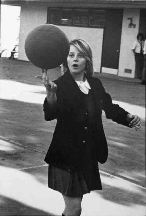 A young Jodie Foster showing off her basketball skills in her school uniform, 1976.